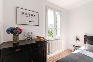 Un dormitorio con cama, cómoda, ventana con vistas, radiador y un cartel enmarcado en la pared.