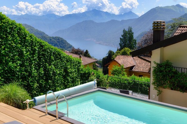 A swimming pool with a view of mountains and a lake, surrounded by greenery and buildings.