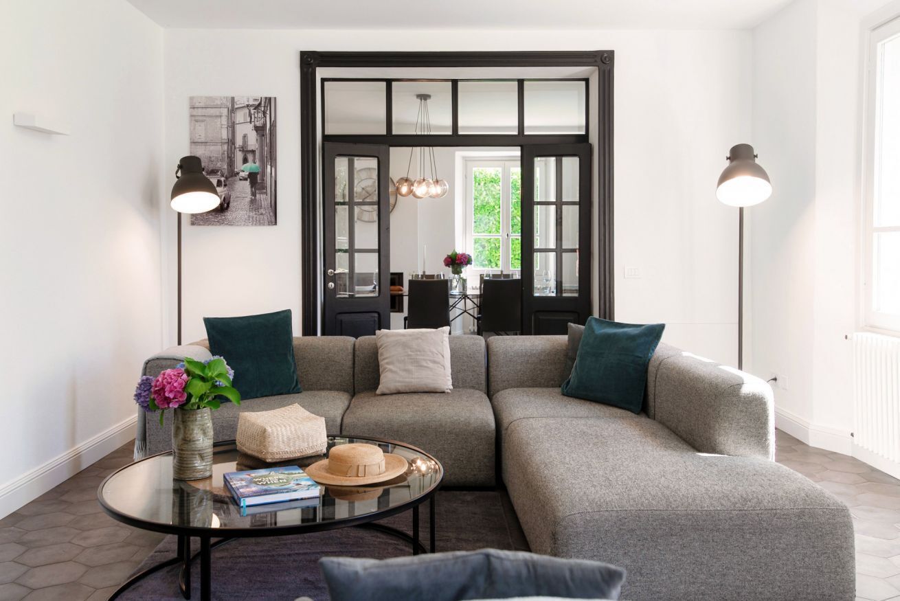 Un salon moderne avec un canapé d’angle, une table basse en verre et une porte à cadre noir offrant une vue dégagée.