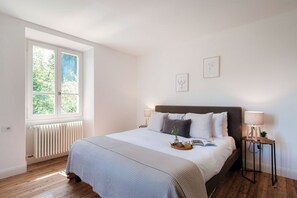 Une chambre avec une grande fenêtre, un lit doté d’une tête de lit, des lampes de chevet et un radiateur.