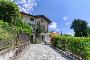 A two-story house with a stone-paved courtyard, a covered seating area, and a fence. - villa Casasco - MyHomeinComo (Casasco d'Intelvi)