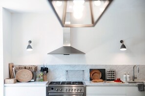 A modern kitchen with a stainless steel stove, two pendant lights, and a range hood. - villa Casasco - MyHomeinComo (Casasco d'Intelvi)