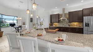 Une cuisine moderne dotée de plans de travail en granit, d’armoires en bois foncé, d’appareils électroménagers en acier inoxydable et de luminaires suspendus.