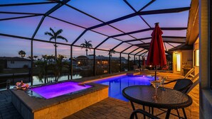 Un espace piscine doté d’une structure en verre, d’un jacuzzi et de coins salon extérieurs.