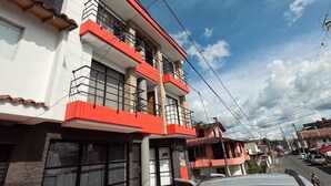Un edificio de varios pisos con fachada roja y blanca, ventanas amplias y entrada con mosaicos.