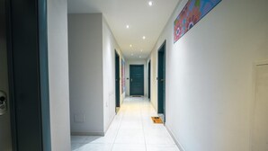 A hallway with white tiled floors, grey walls, and a blue door at the end. - Turin Airport apartment G (Leinì)