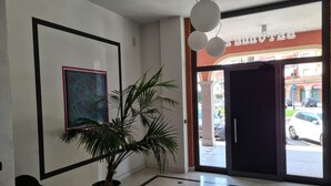 A lobby with a potted plant, a framed abstract painting, and a view of the street outside. - Turin Airport apartment G (Leinì)