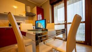 A modern kitchen with red cabinets, a glass dining table, and a laptop displaying a building image. - Turin Airport apartment G (Leinì)