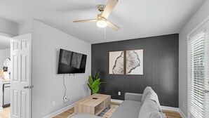 Een moderne woonkamer met een grijze bank, een houten salontafel, een plafondventilator en kunst aan de muur.