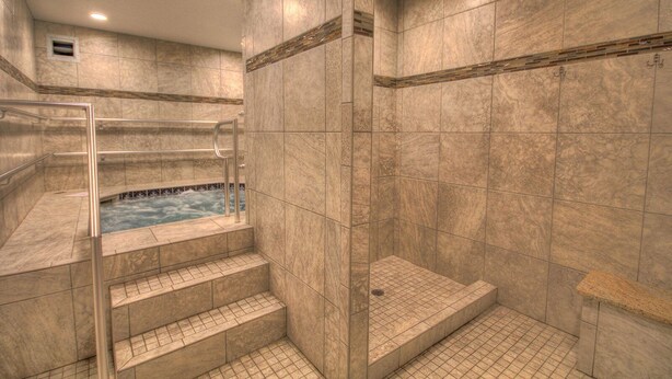 Un área de spa con un jacuzzi, paredes de azulejos y una ducha con cerramiento de vidrio.