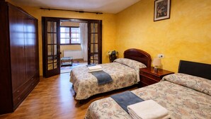 Een hotelkamer met twee bedden, houten vloeren, een ruime kledingkast en uitzicht door een open deur.
