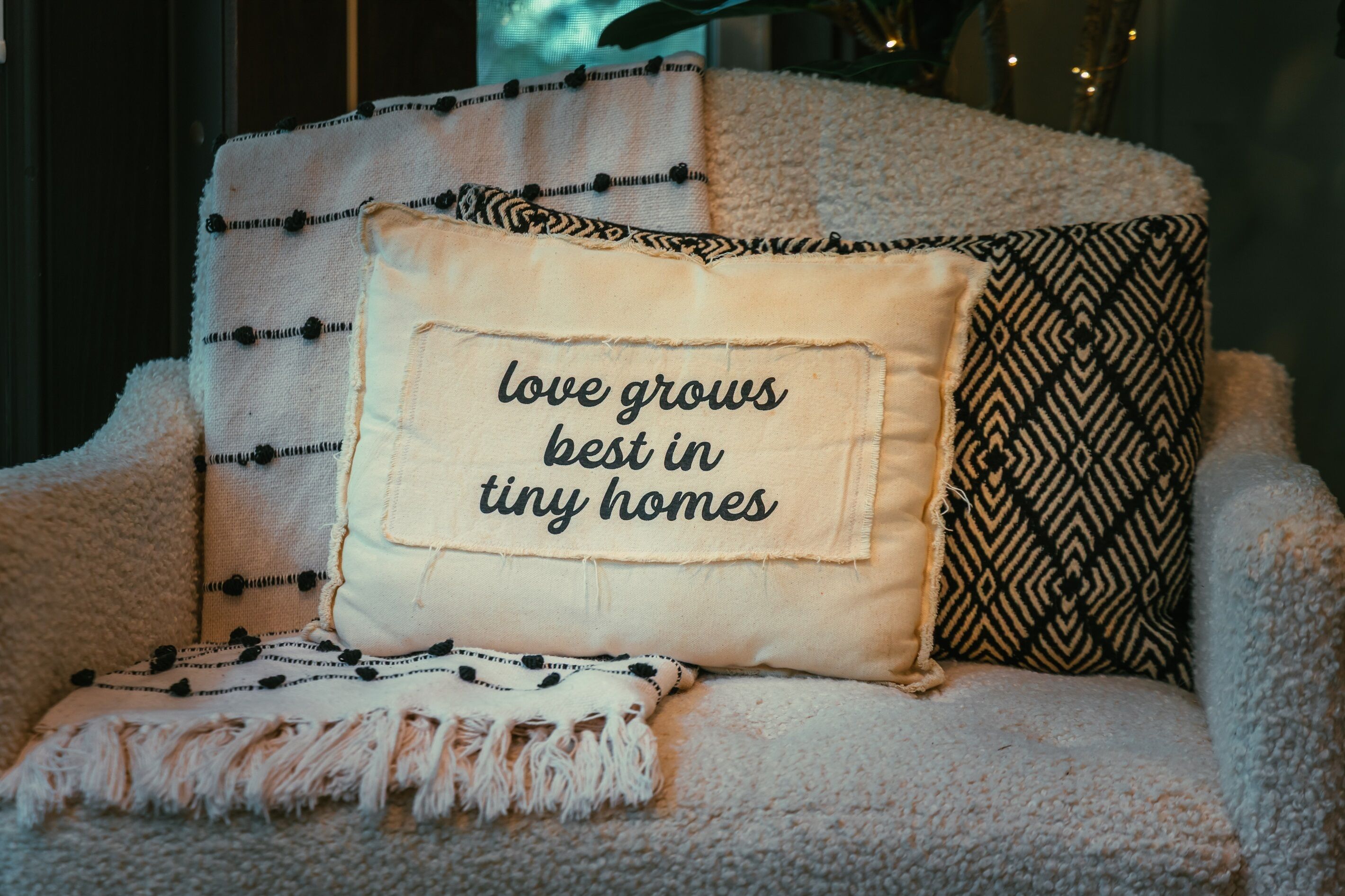 Ein gemütliches Wohnzimmer mit einer Couch, einer Decke und dekorativen Kissen mit einem motivierenden Spruch.