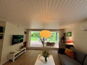 Un salon moderne dotĂ© dâun tĂ©lĂ©viseur Ă Ă©cran plat, dâune table basse ornĂ©e de fleurs, dâun canapĂ© et dâun coin repas avec des chaises et une table.