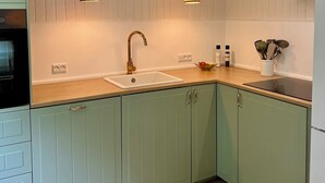 Una cocina con gabinetes verde claro, una encimera blanca, un fregadero, dos lámparas colgantes y una estufa.