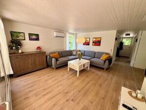 A living room with a sofa, a coffee table, and a cabinet. There are framed pictures on the wall and a window with curtains.