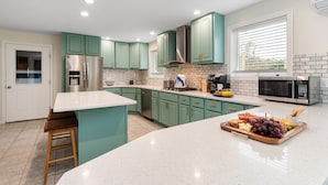 A modern kitchen with teal cabinets, stainless steel appliances, and a central island with a fruit platter.