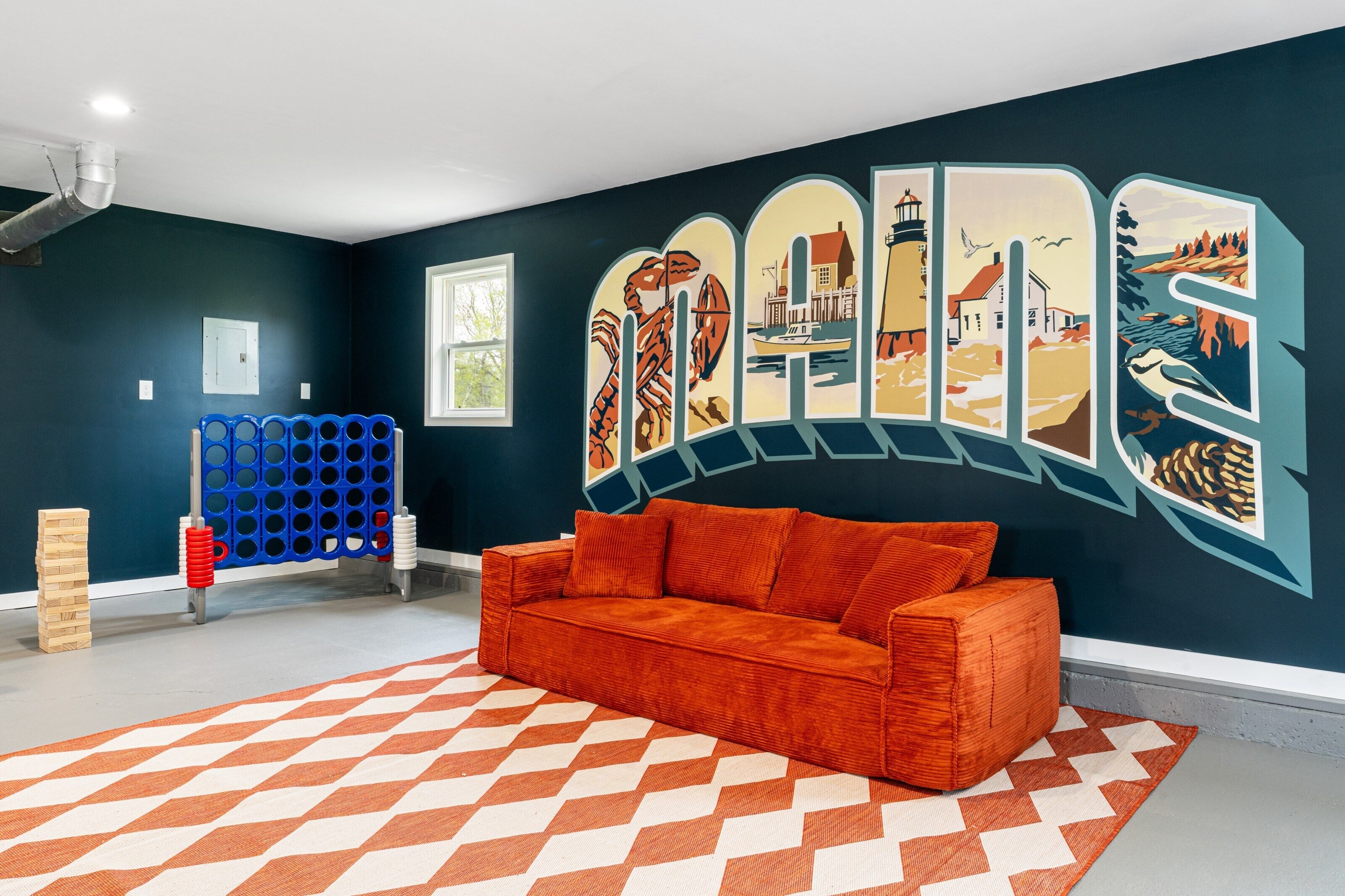 A room with a dark blue wall, a red sofa, a patterned rug, and a blue and red play structure.