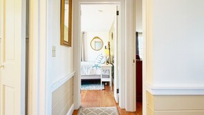 Un couloir menant à une chambre à coucher équipée d’un lit, d’une table de chevet et d’un miroir.