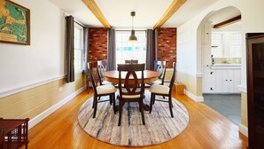 Un coin repas avec une table ronde, des chaises et un tapis. Un mur en briques et des poutres en bois ornent le plafond.