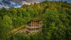 Una cabaña de troncos de varios pisos con un balcón, rodeada de un bosque frondoso.