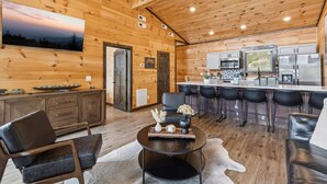 Amplio interior de cabaña con detalles de madera, una zona de cocina y un área de estar con una mesa redonda y sillas.