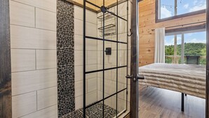 Un baño moderno con cabina de ducha de vidrio, pared decorativa de piedra y suelo de madera.