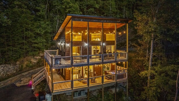 Una cabaña de madera de varios niveles con paredes de vidrio, un balcón y luces colgantes.