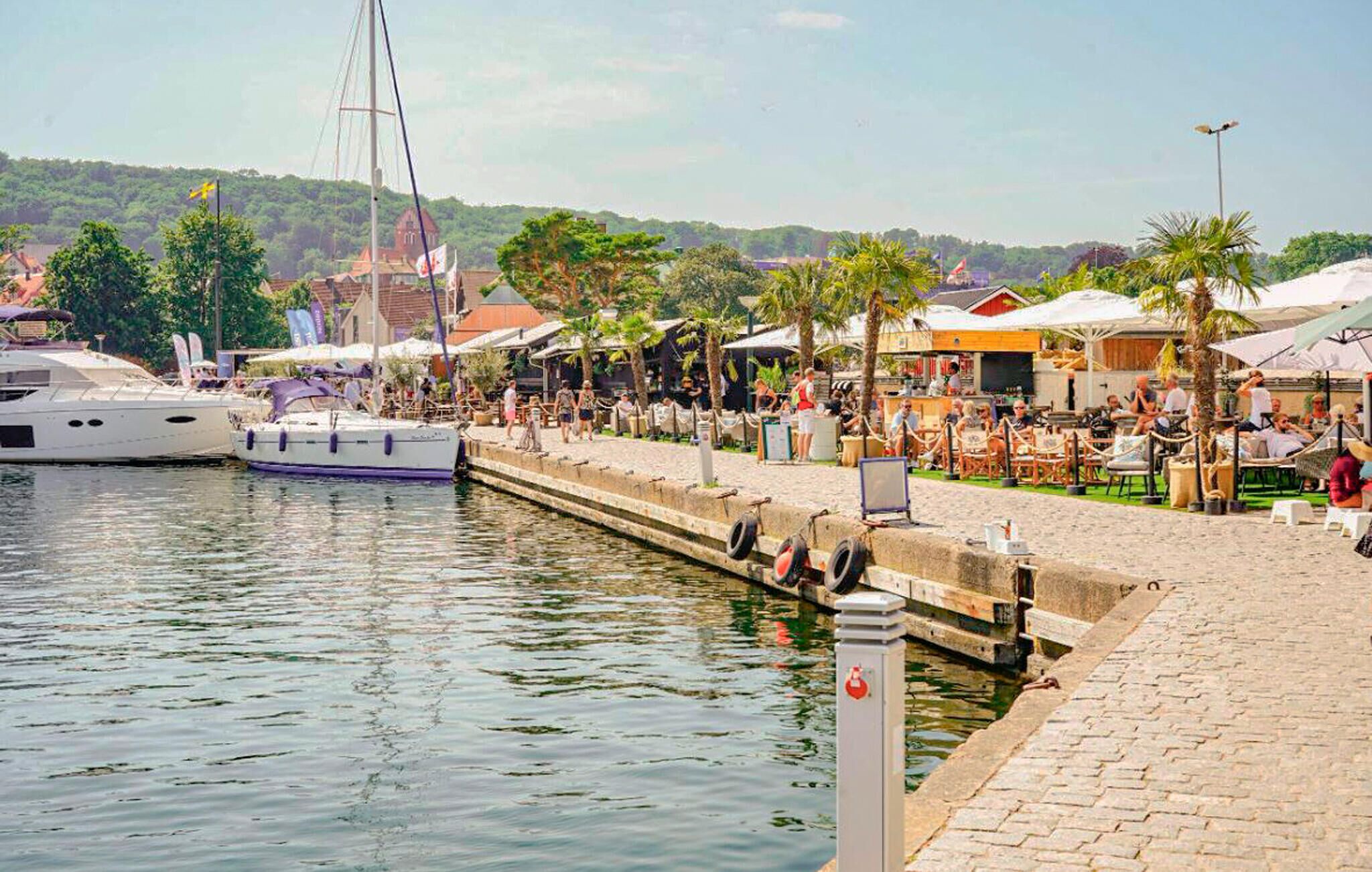 A marina with boats docked, a paved walkway, and outdoor seating areas with umbrellas.