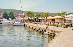 Un port de plaisance avec des bateaux amarrés, une promenade pavée et des espaces de détente en plein air dotés de parasols.