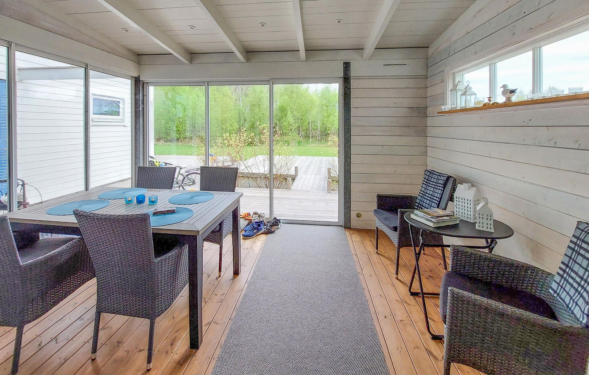 Katettu terassi, jossa on pöytä ja tuoleja, näkymä ulos ja puinen terassilattia.