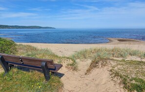 A bench overlooking a beach with a clear view of the sea and distant hills.