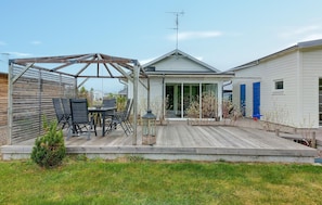 A house with a covered patio, a dining area with chairs and a table, and a garage with blue doors.