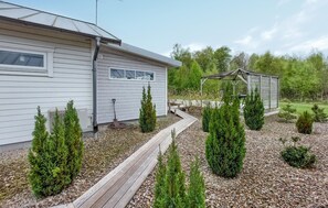 Une maison moderne dotée d’une terrasse en bois, d’un espace salon extérieur abrité et d’un jardin avec de jeunes arbres.