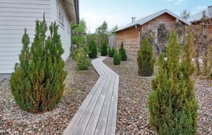 A wooden pathway leading to a cabin with a sloped roof, surrounded by evergreen shrubs and a gravel bed. - 1 bedroom cozy home in Skummeslöv (Skummeslöv)