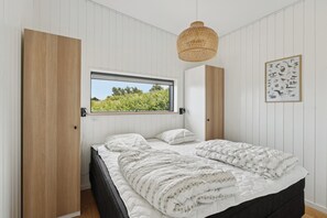 Une chambre avec une grande fenêtre, un lit recouvert d’une couette à motifs, un luminaire suspendu et un tableau représentant des oiseaux accroché au mur.
