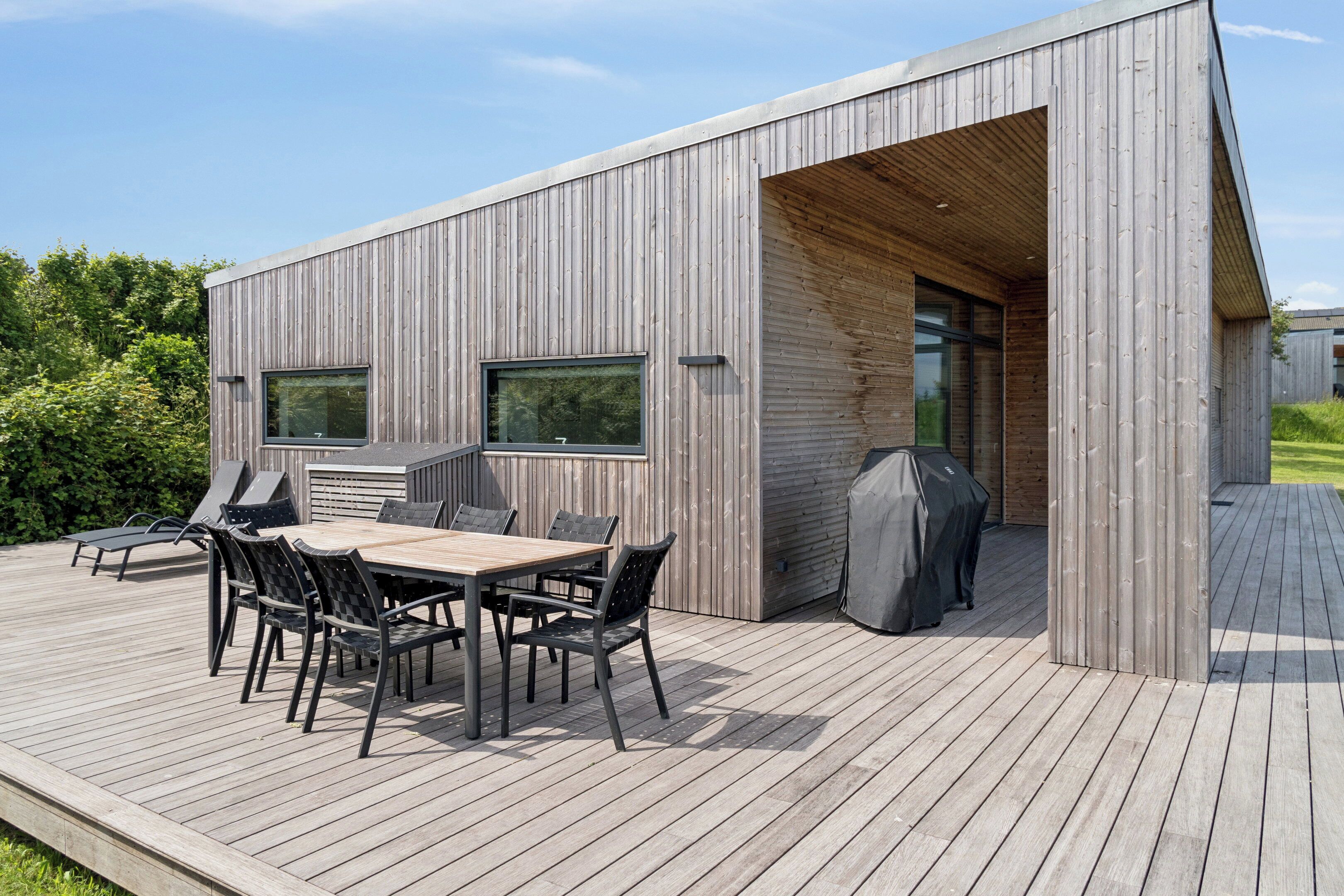 A modern wooden building with a deck, a barbecue grill, and a covered seating area.