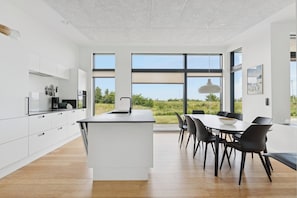 Une cuisine moderne dotée d’un îlot central, de meubles blancs et d’un coin repas avec des chaises noires.