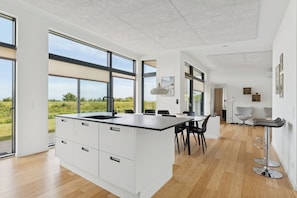 Une cuisine moderne dotée de grandes fenêtres, d’un îlot central et d’un coin repas avec des chaises.
