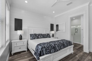 Un dormitorio con cama, mesitas de noche y un baño visible a través de una puerta de cristal.