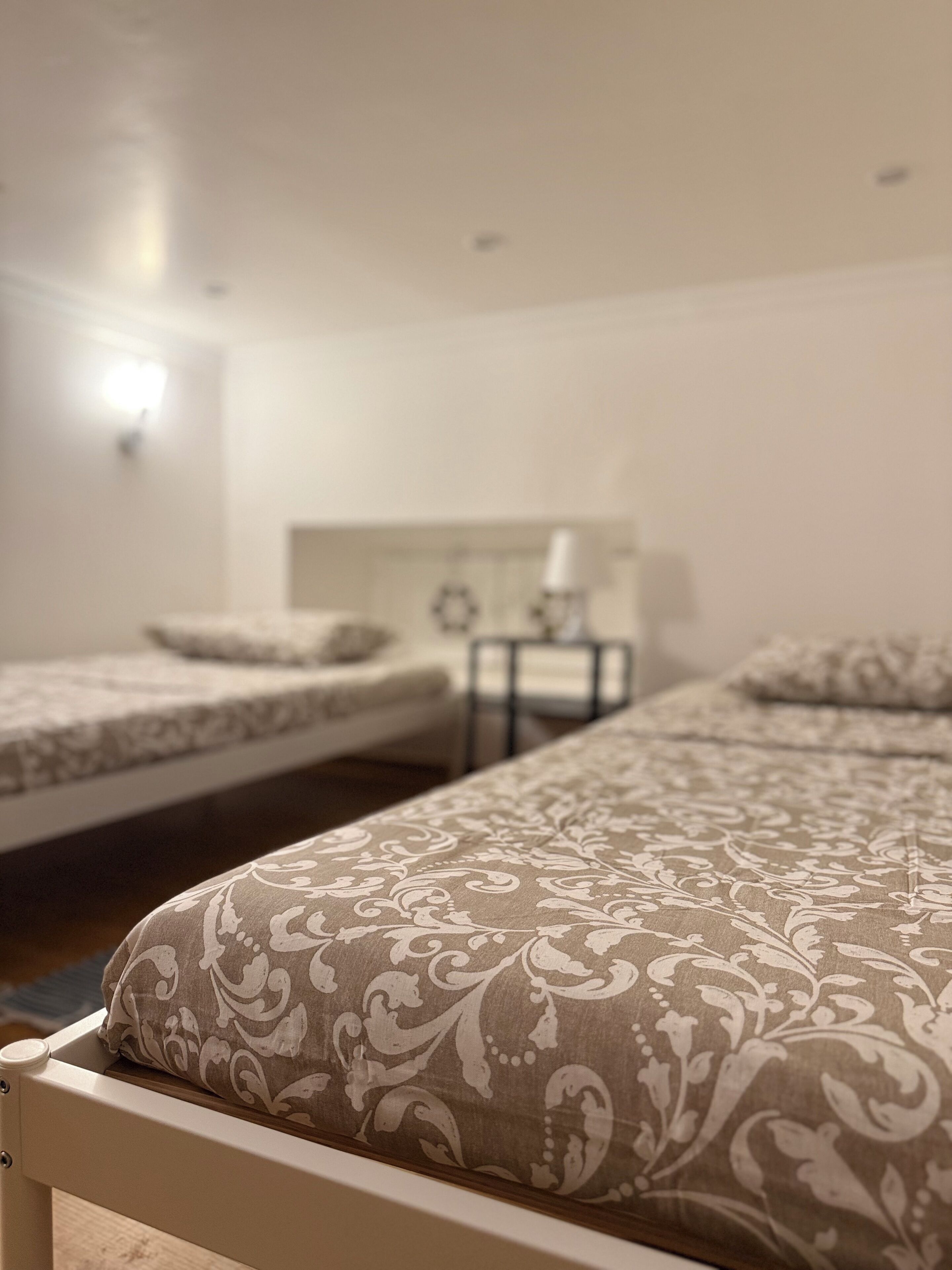 Una habitación de hotel con dos camas individuales, una mesita de noche con lámpara y una lámpara de pared.