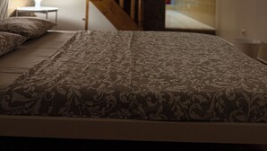A bedroom with a bed, a nightstand, a lamp, a wooden staircase, and a view of a hallway. - Faro Coast Guest House (Faro)