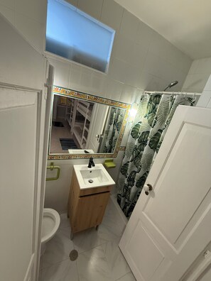 A bathroom with a white sink, a mirror, a toilet, and a shower curtain with a leaf pattern. - Faro Coast Guest House (Faro)