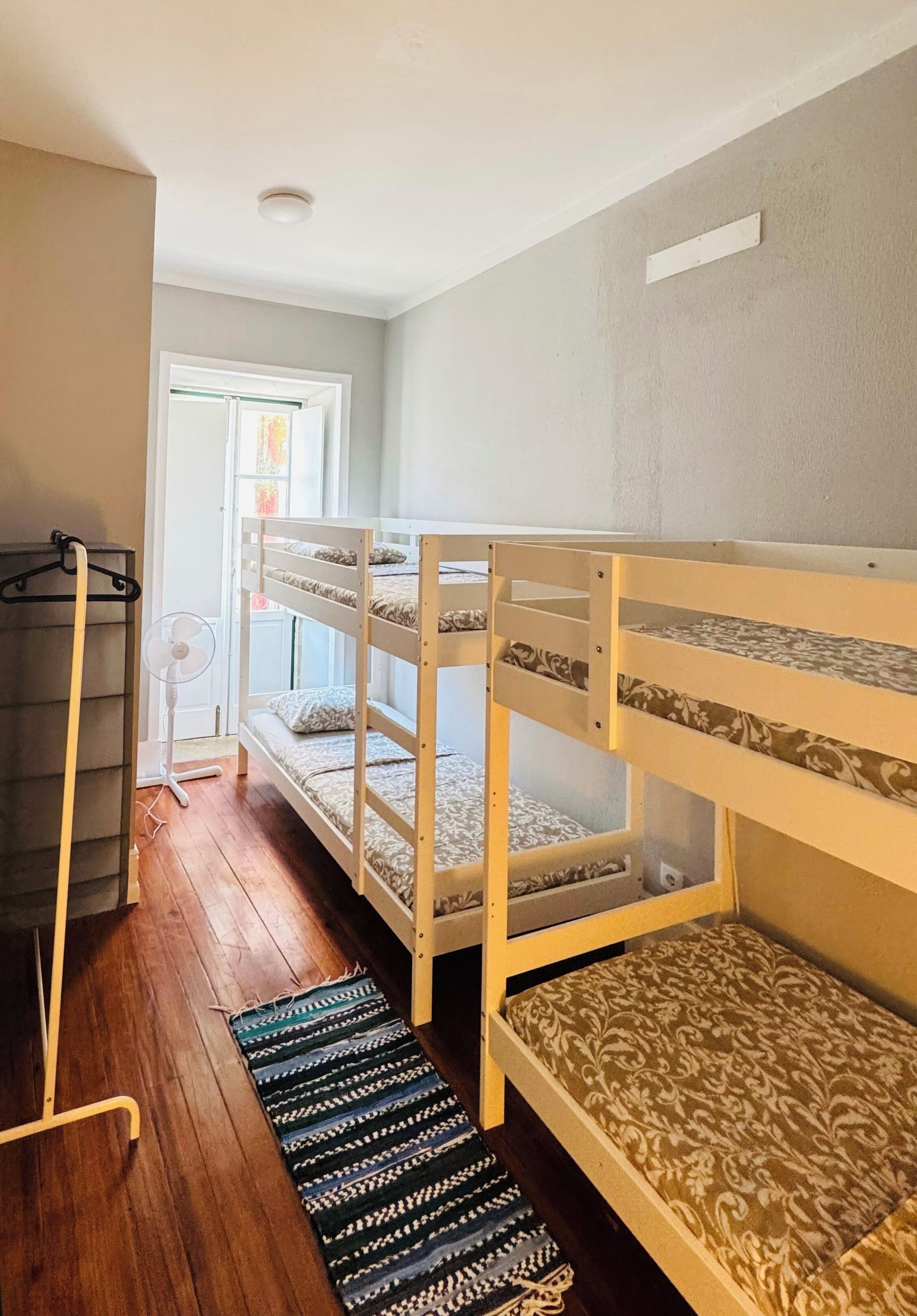 A room with bunk beds, a fan, a coat rack, and a patterned rug.
