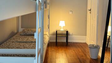 A room with bunk beds, a small table with a lamp, a trash bin, and a door with a sign.