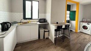 A compact kitchen with a microwave, kettle, and sink. There's a small dining area with stools and a washing machine in the corner. - Faro Coast Guest House (Faro)