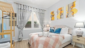 Un dormitorio con cama, una silla de madera, una mesita de noche y una ventana con cortinas.