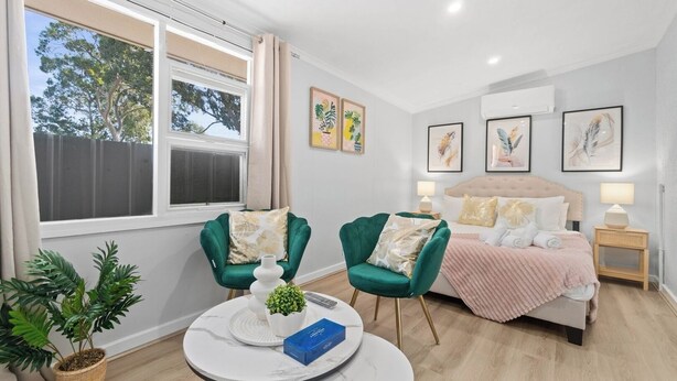 Un dormitorio moderno con una cama, dos sillones verdes, una mesa redonda y una planta en maceta.