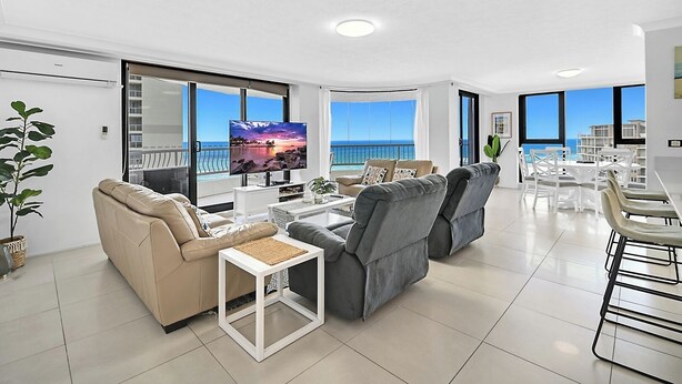 A modern living room with a large TV, comfortable seating, and a view of the ocean. - Stunning Ocean View 3BR near Broadbeach | Parking (Surfers Paradise)