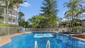A swimming pool with lounge chairs, surrounded by palm trees and a fence. - Stunning Ocean View 3BR near Broadbeach | Parking (Surfers Paradise)