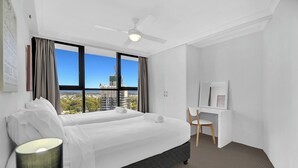 A hotel room with a bed, a desk, a chair, a lamp, and a view of the city. - Stunning Ocean View 3BR near Broadbeach | Parking (Surfers Paradise)